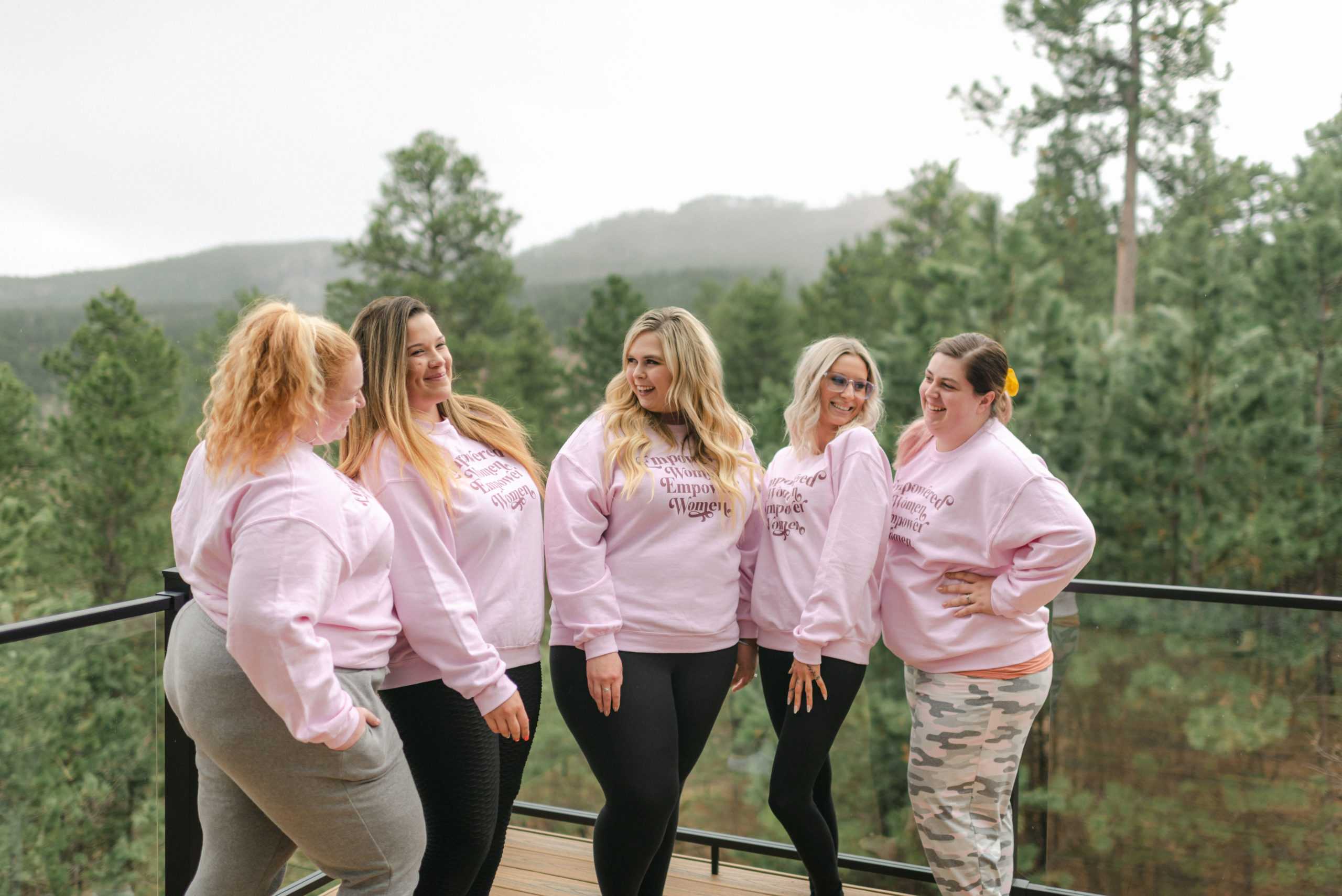 five women wearing matching pink sweatshirts with a forest behind them