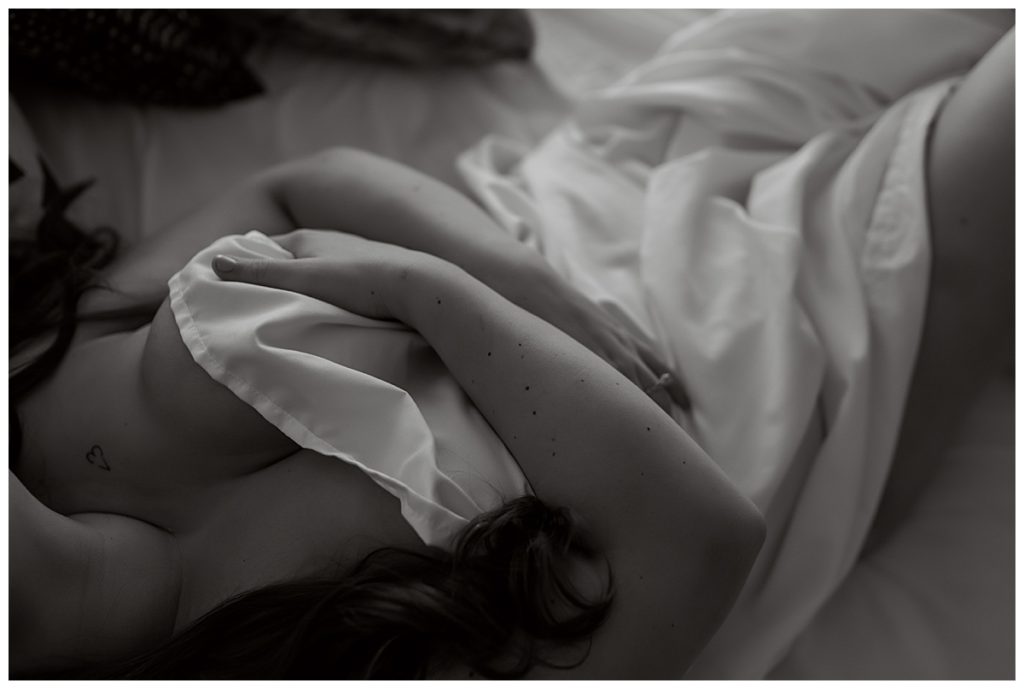 Sheet covering woman laying on bed by Emma Christine Photography