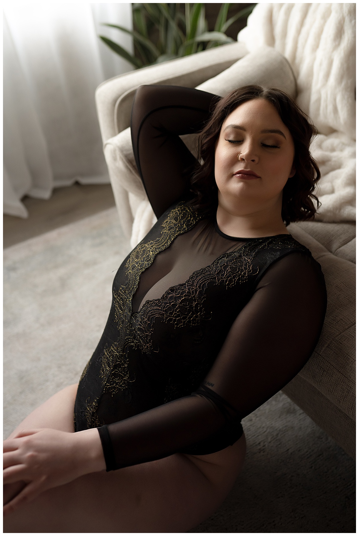 A woman leans against couch in black lingerie and suggests to Book Your Boudoir Session