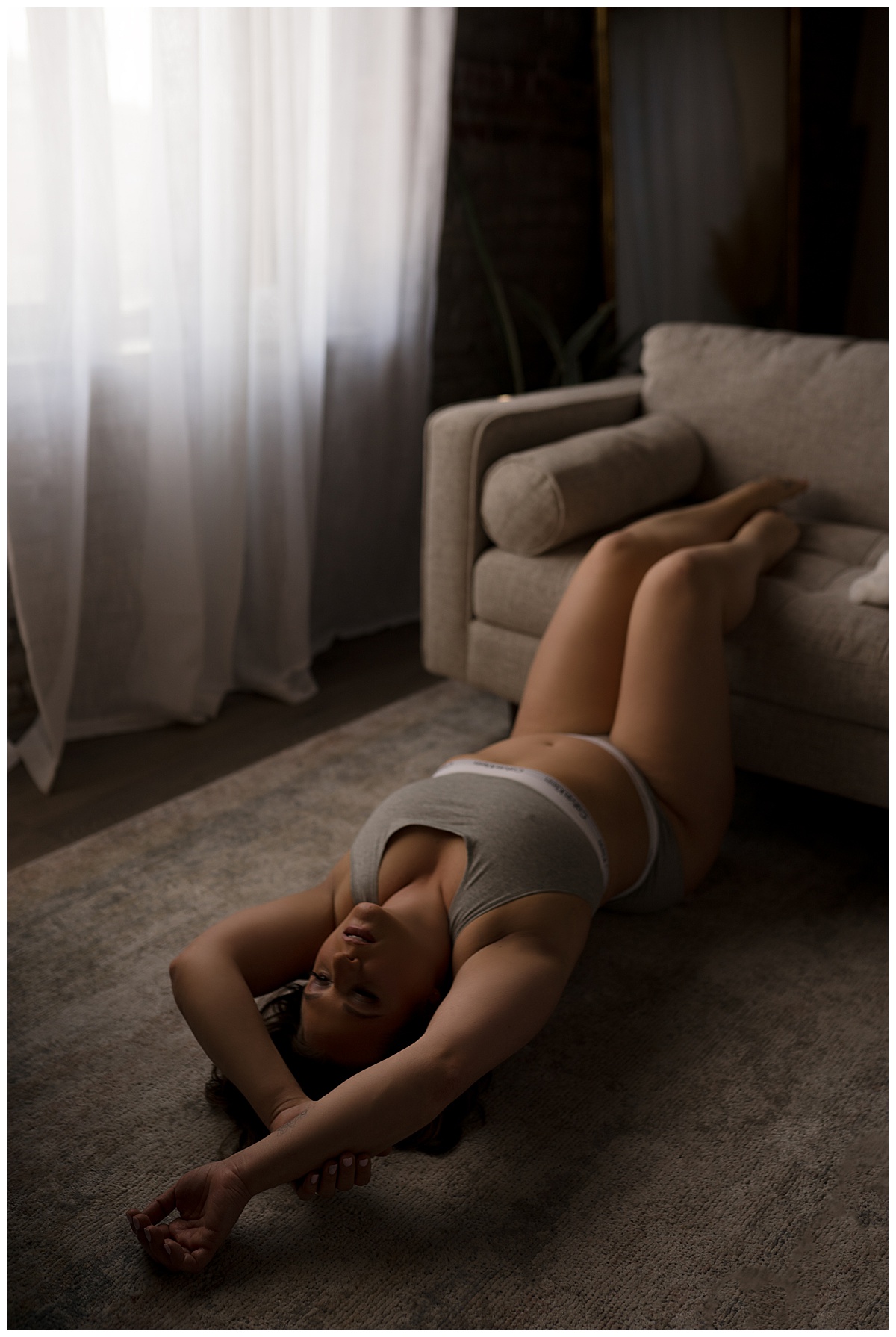 Woman holds feet on couch and lays on floor for Sioux Falls Boudoir Photographer