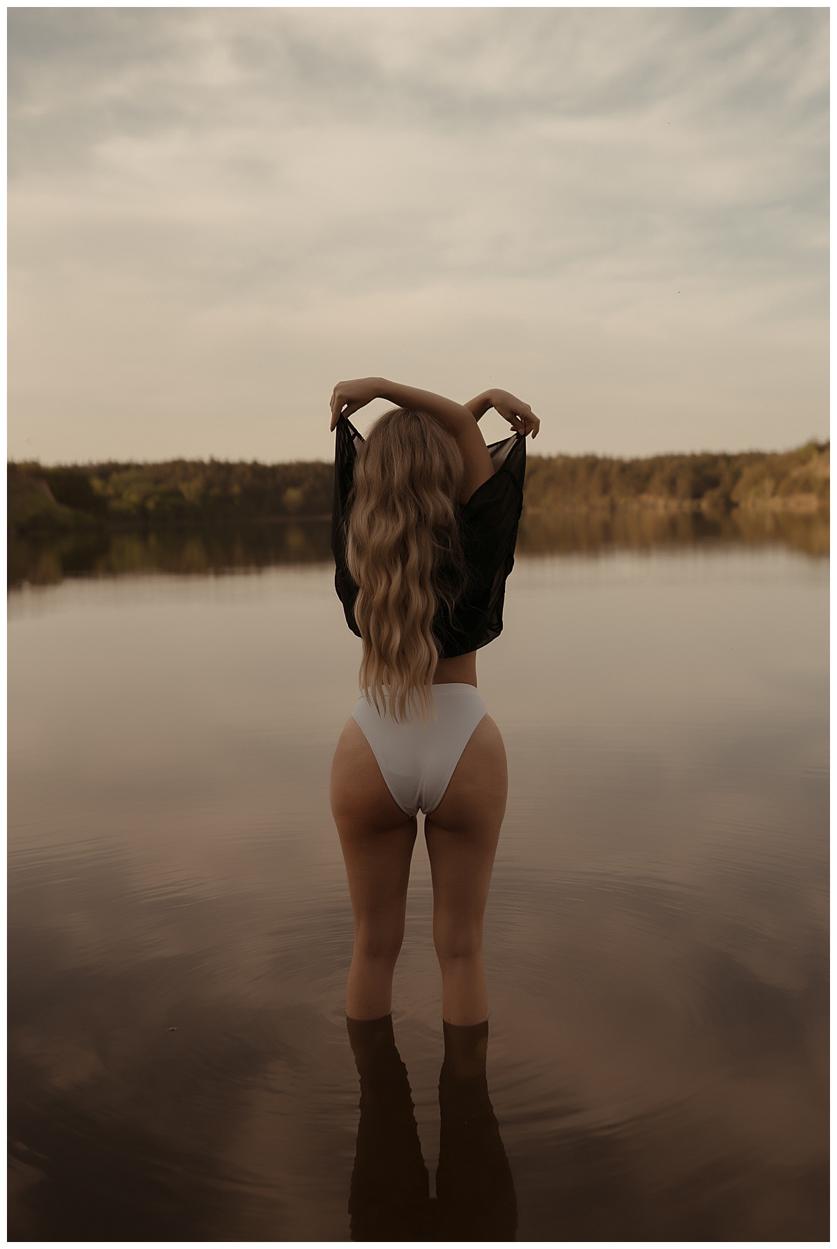 Person pulls shirt off standing in the water wearing white lingerie for Sioux Falls Boudoir Photographer
