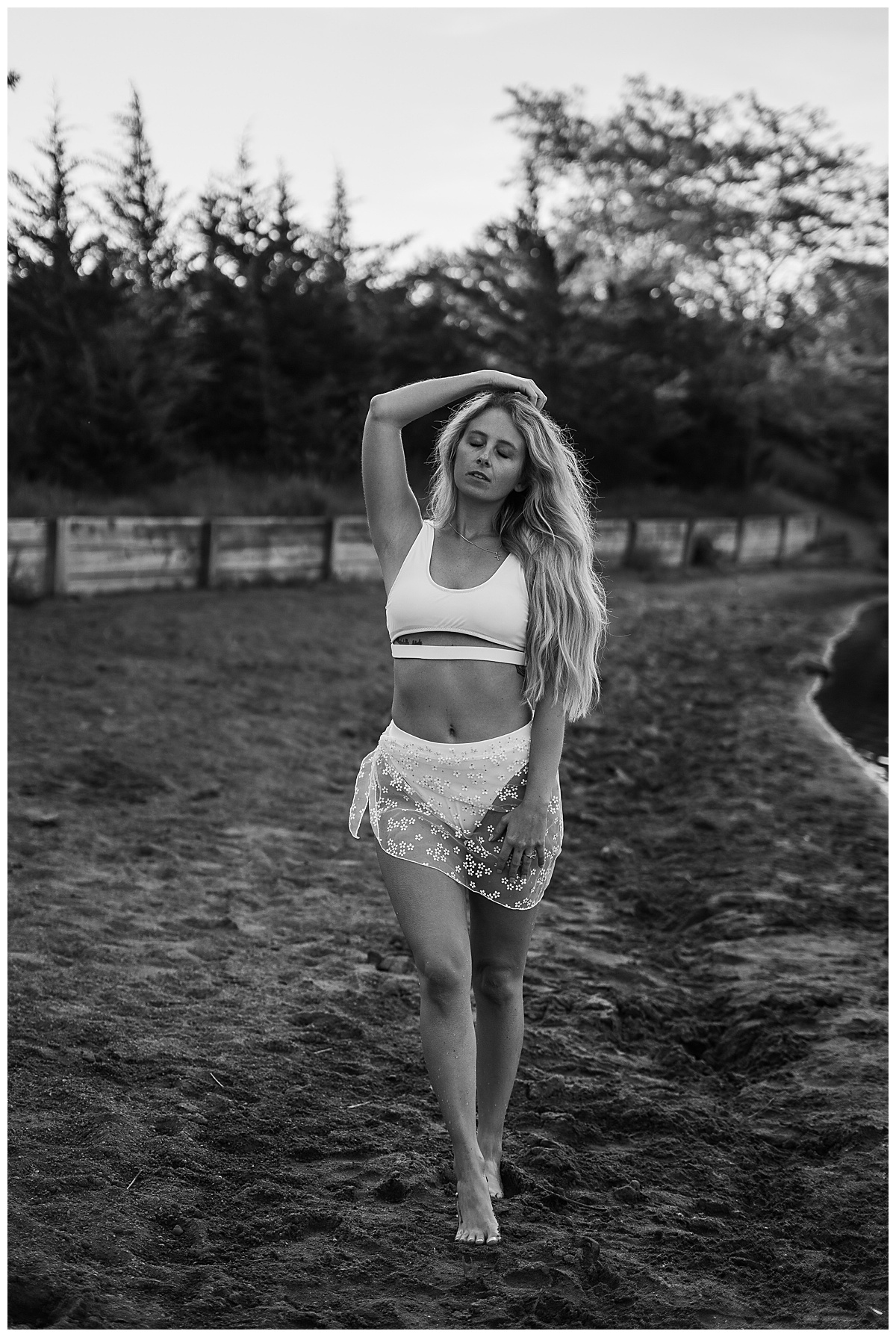 Adult walks in the sand wearing white lingerie for lakeside boudoir session