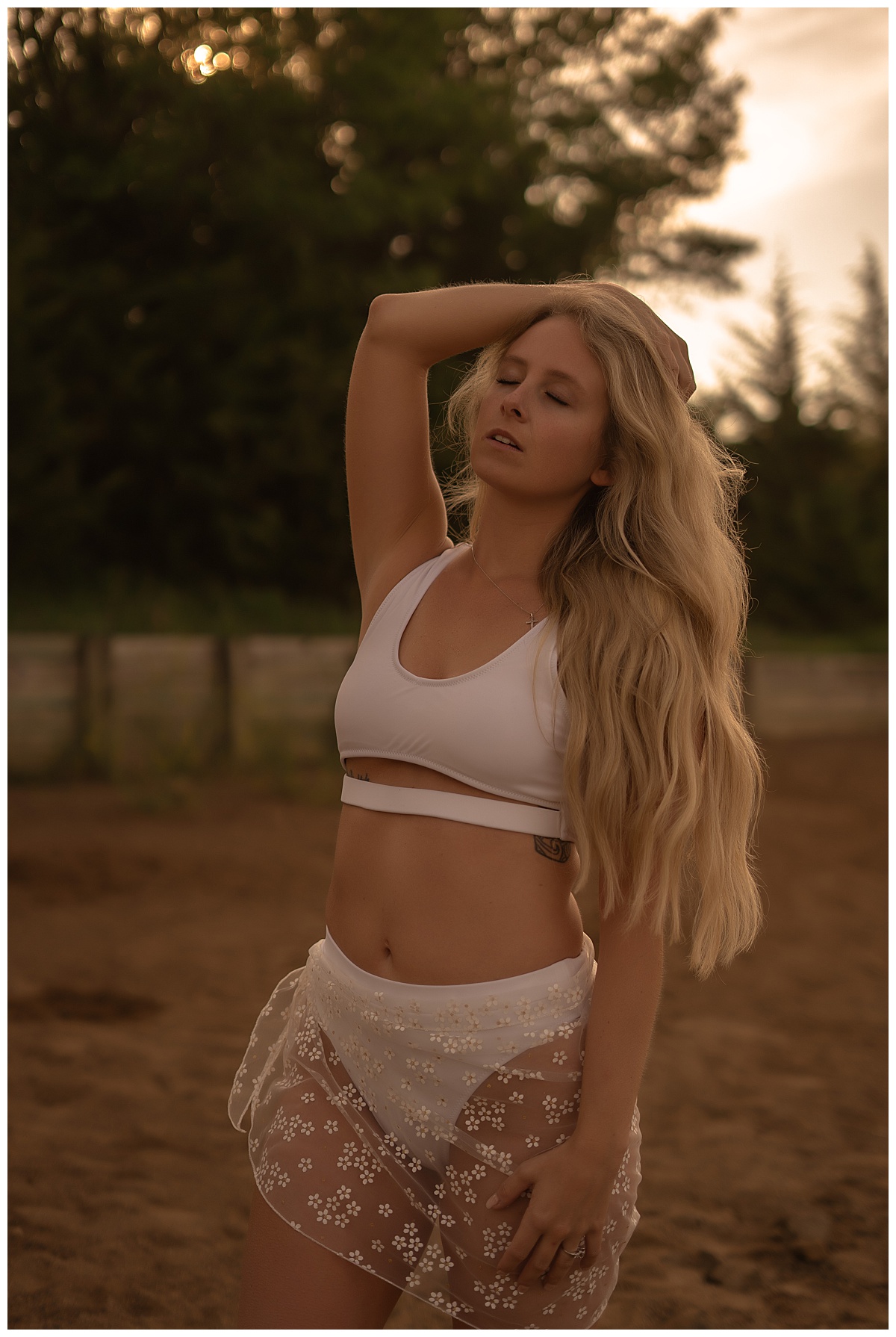 Girl runs fingers through hair wearing white lingerie for lakeside boudoir session