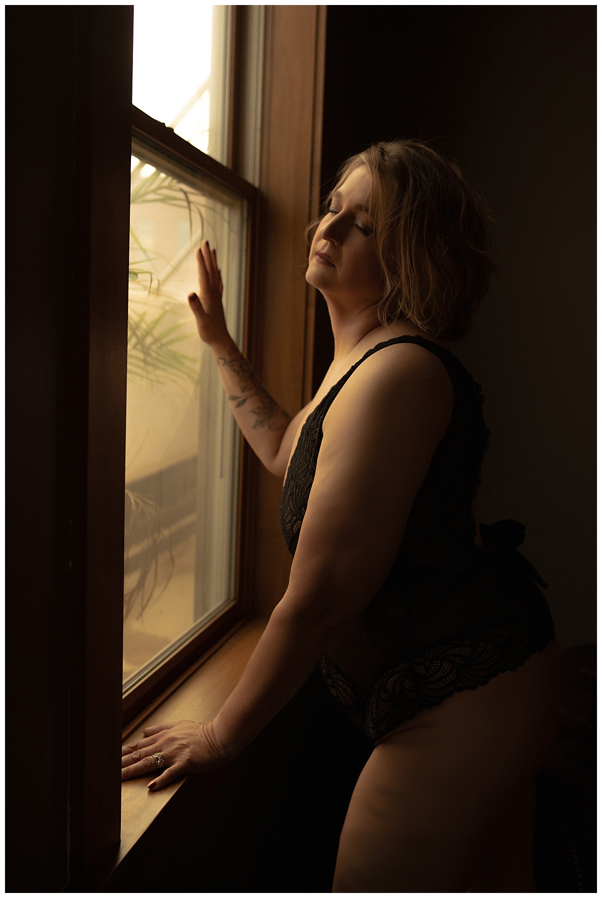 Girl sits in front of window wearing lingerie for Sioux Falls Boudoir Photographer