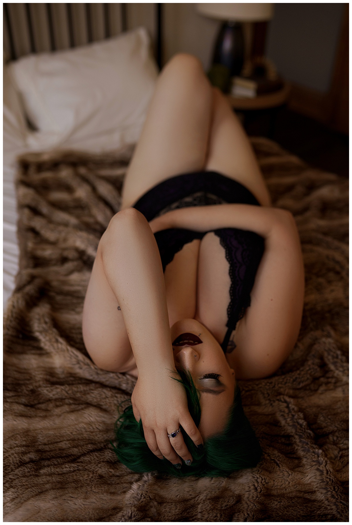 Woman lays on the bed holding her had to her head for Sioux Falls Boudoir Photographer