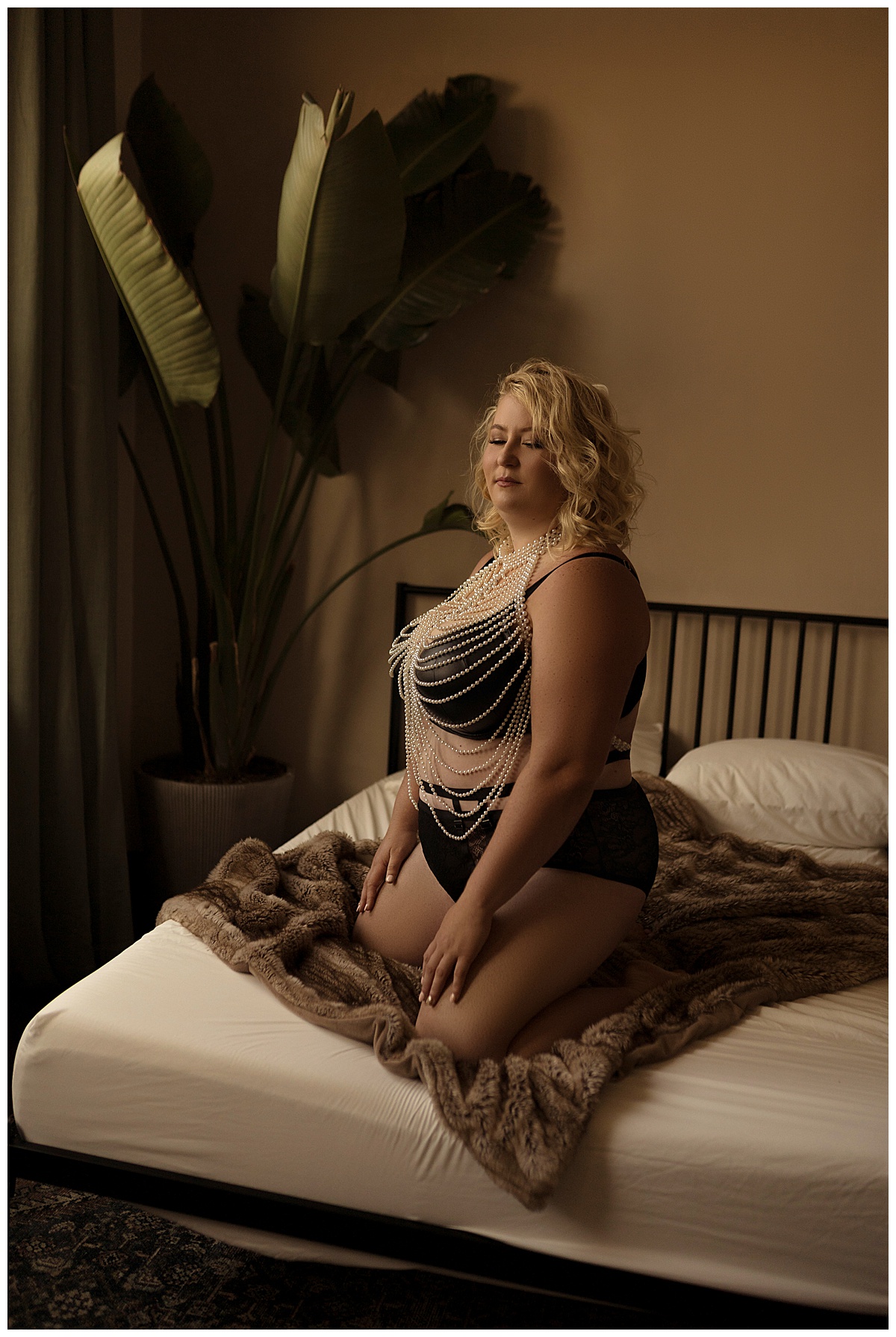 Adult kneels on the bed wearing black lingerie and wearing body jewelery for Emma Christine Photography