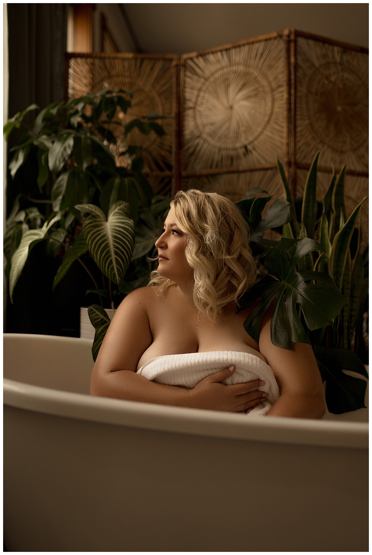 Female sits in a tub covering her chest for Sioux Falls Boudoir Photographer after wearing a corset 