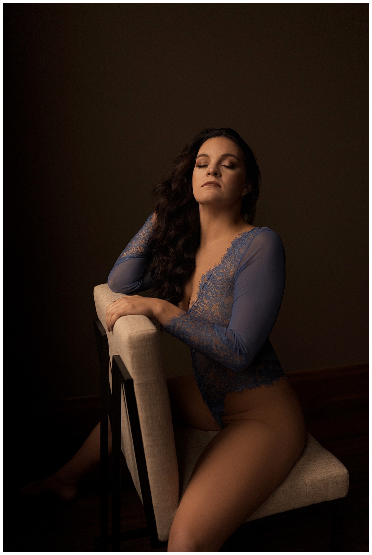 Girl sits on the chair wearing blue lingerie and closes her eyes to calm the nerves during her boudoir session