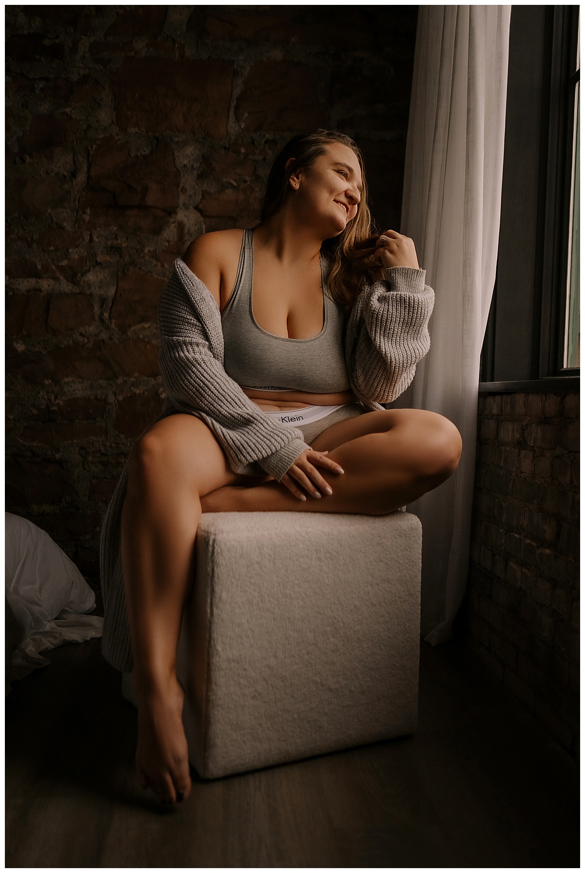 Person sits on a stool wrapped in a cozy cardigan for Emma Christine Photography