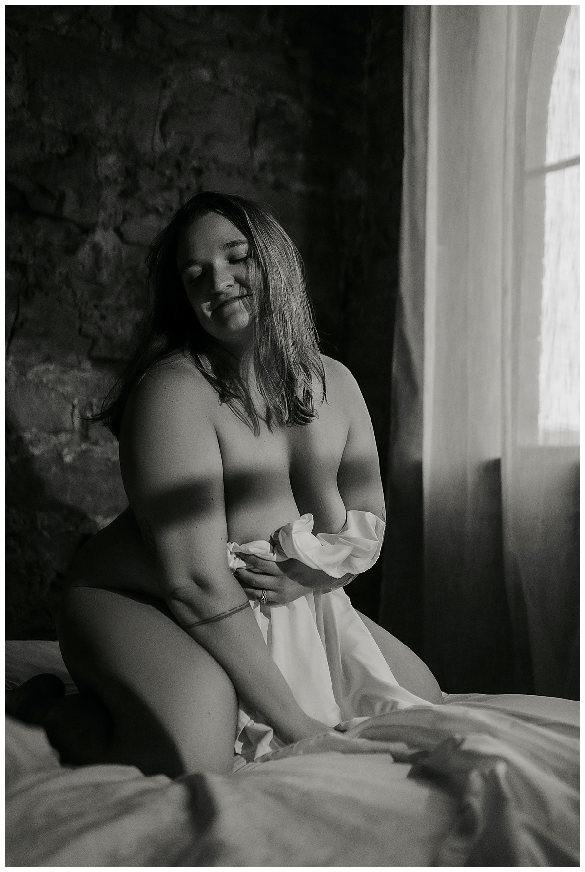 Adult covers her chest with a sheet during her cozy boudoir session