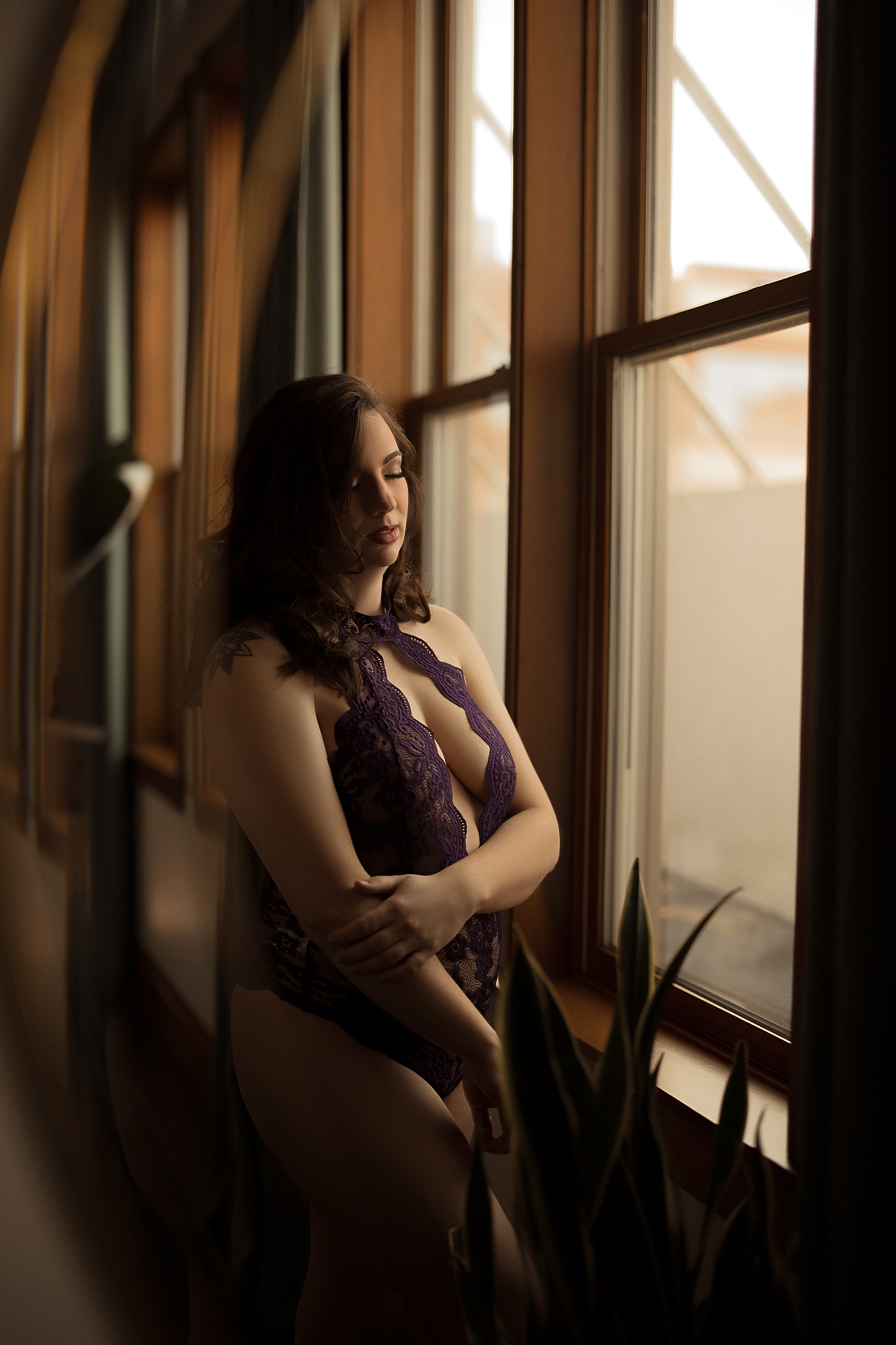 woman stands by large window in studio by Emma Christine photography