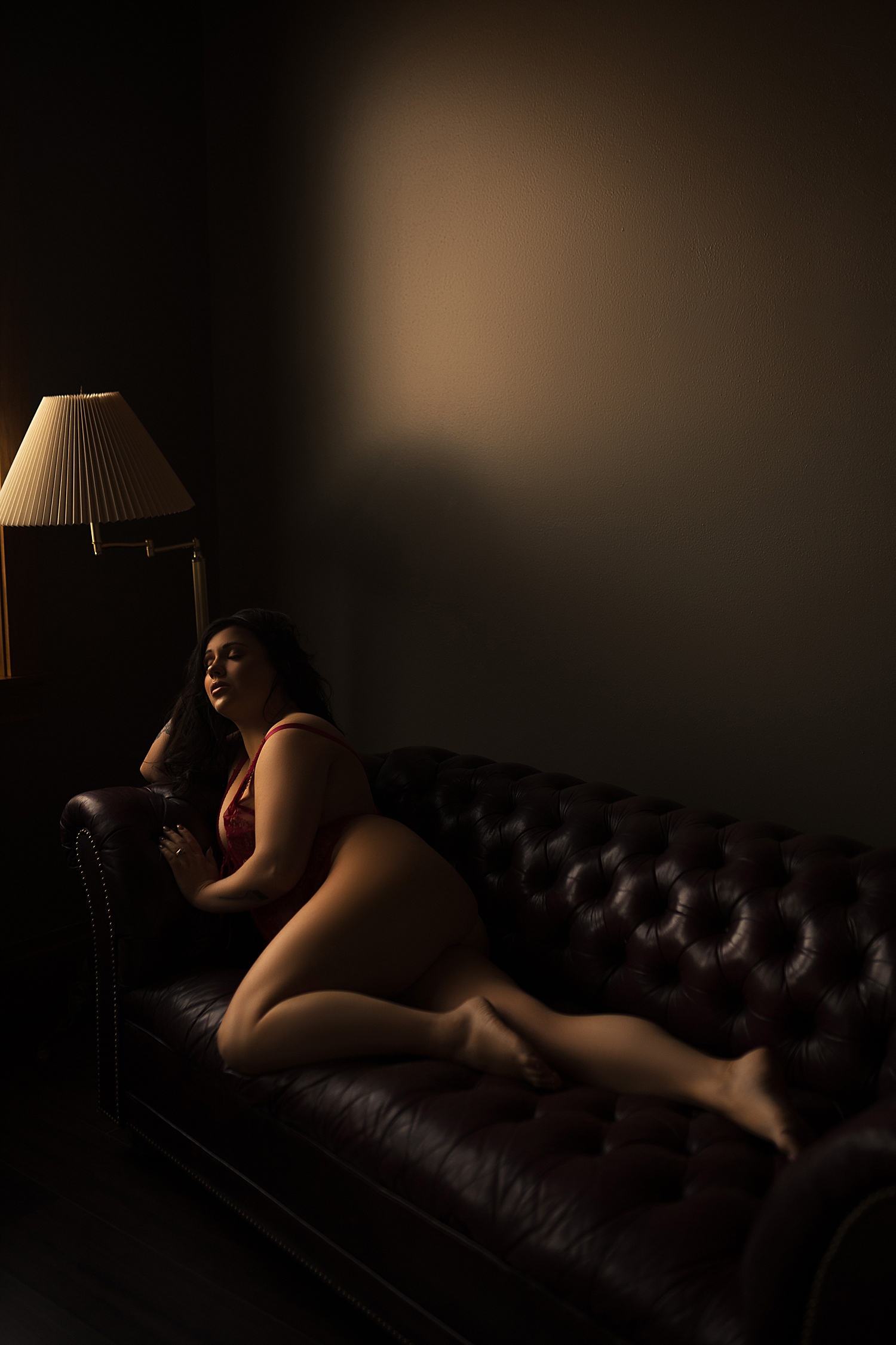 brunette with long legs lies across leather couch by Sioux Falls boudoir photographer