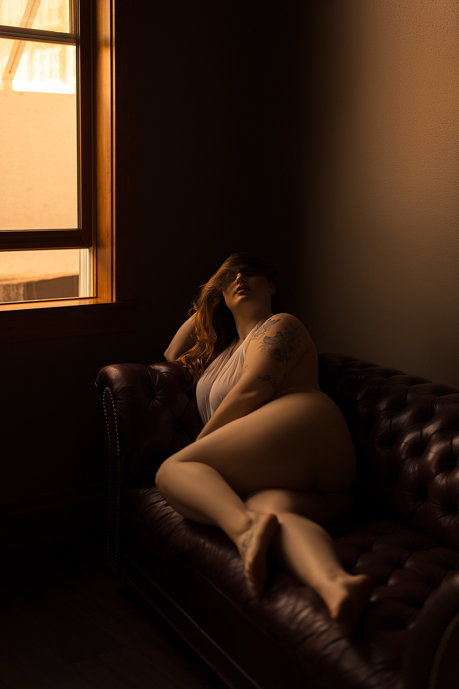 person lies across the couch in white bodysuit by Emma Christine photography
