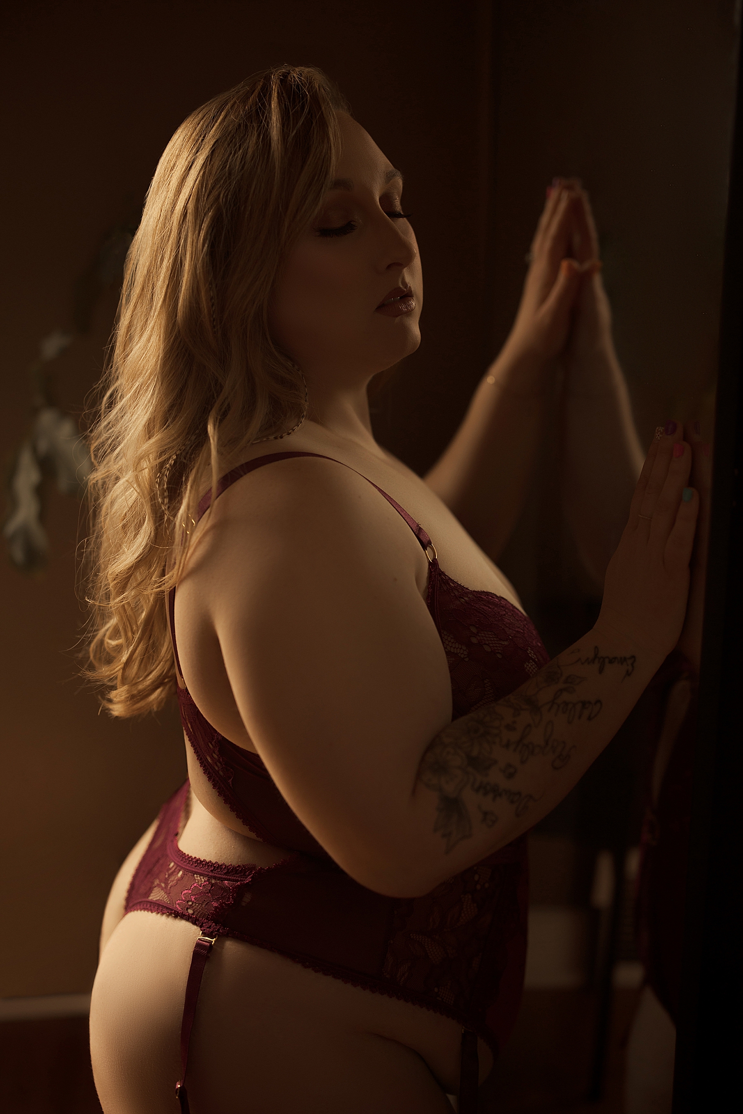 blonde woman with tattoos leans into mirror by Emma Christine Photography