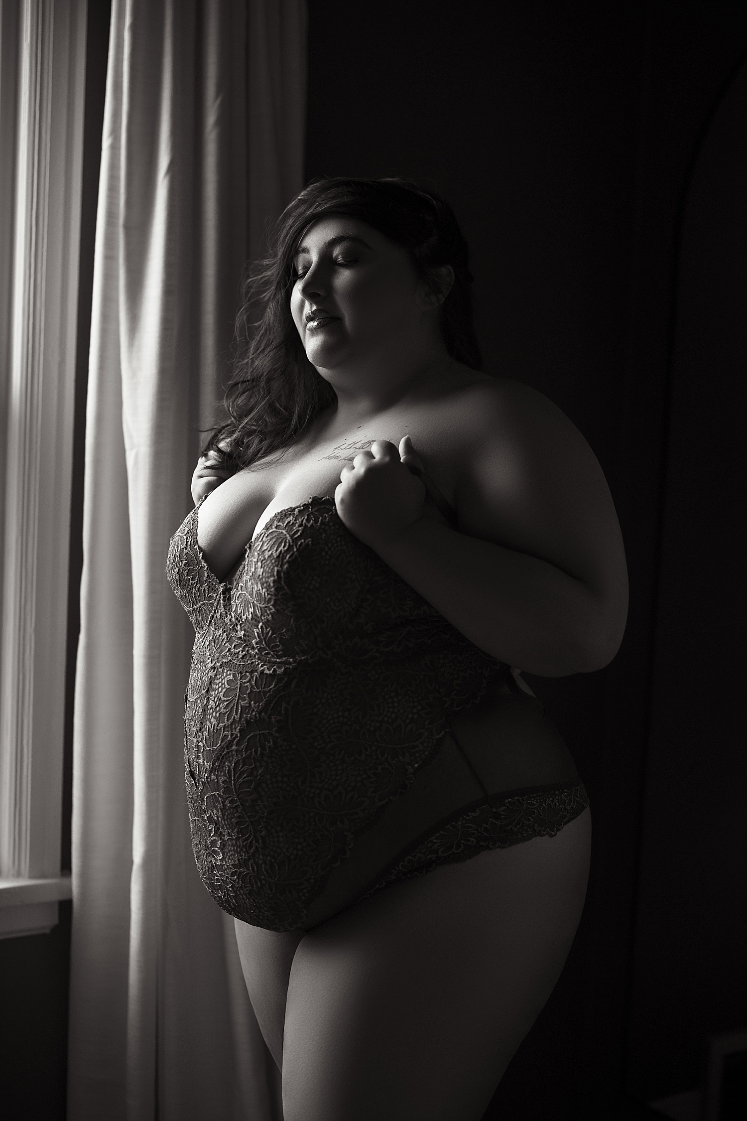 beautiful model stands in front of window in lace bodysuit by Sioux Falls Boudoir Photographer