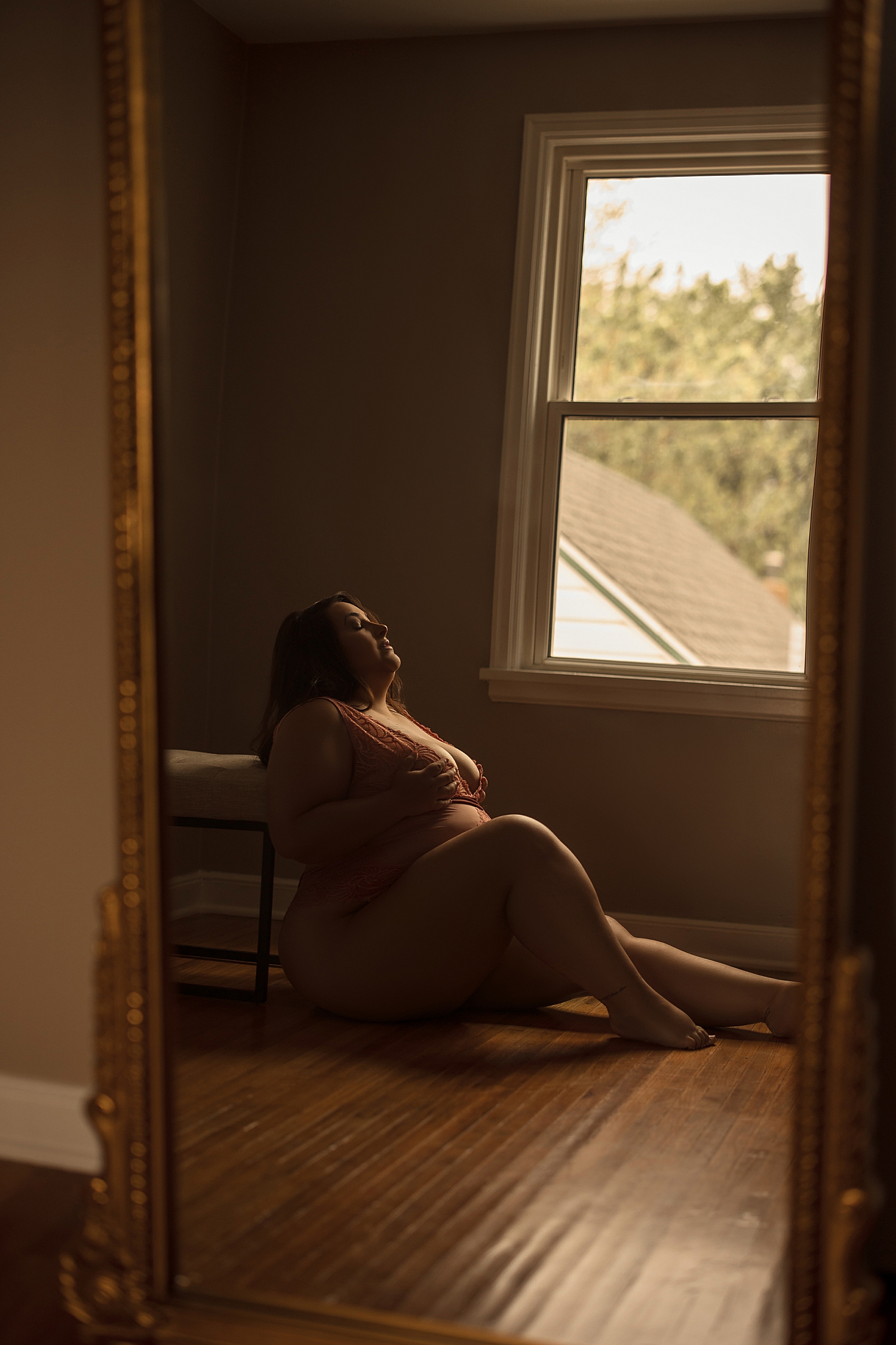woman sits on studio floor under a window in lingerie despite insecurity 