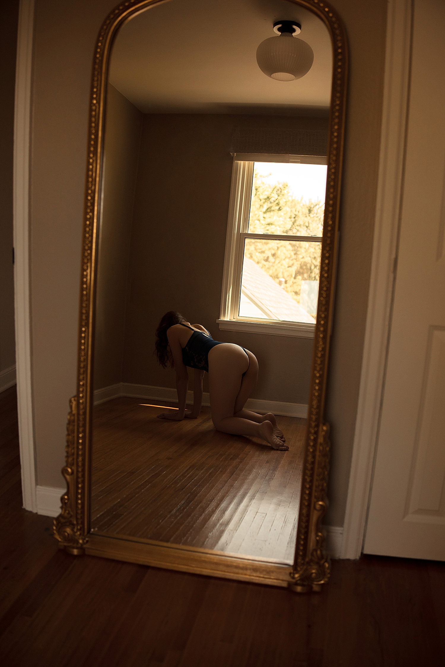 person in blue bodysuit kneels on wood floors in front of mirror by Sioux Falls Boudoir Photographer